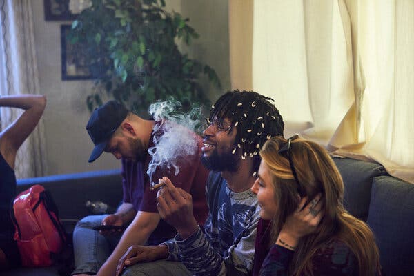 Guests laugh as they sit around and smoke marijuana.